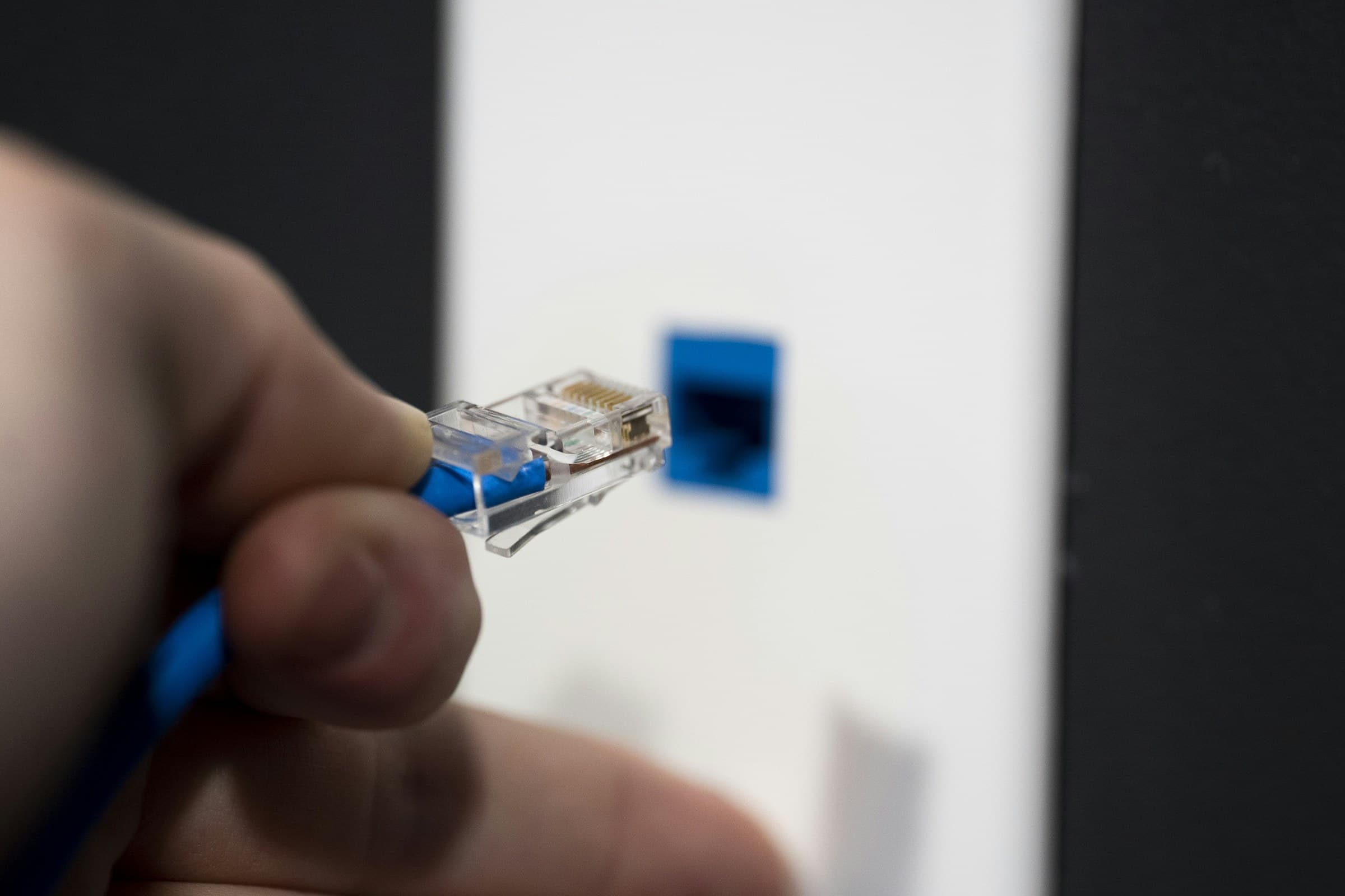 Eine Hand steckt ein blaues Netzwerkkabel in die Wanddose